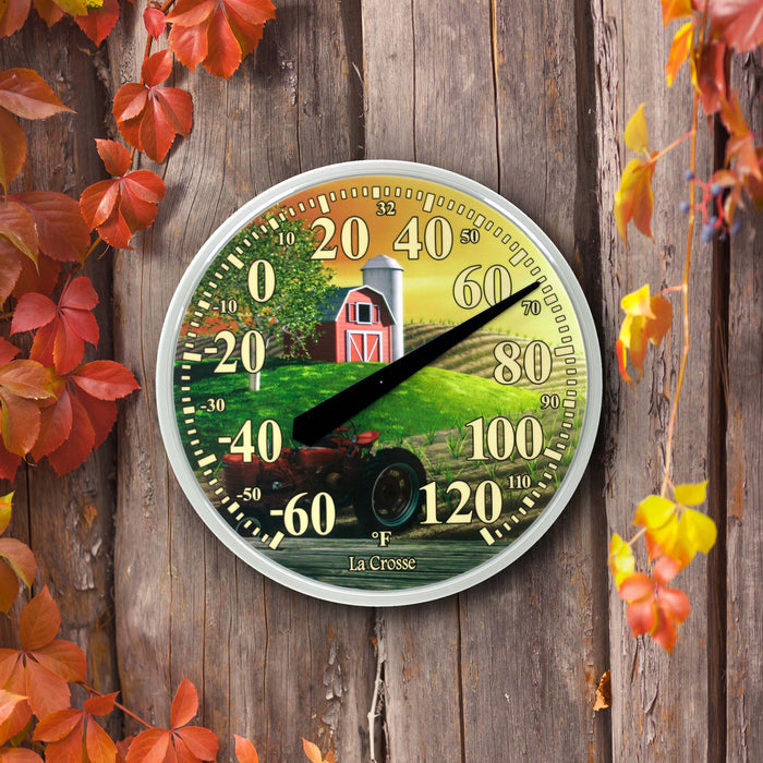 Lifestyle image of the 104-114-FARM 13.5-inch Dial Thermometer - Barn, with key hider, temperature scale in Fahrenheit -60 to 120 degrees with a red-tipped pointer in a white slimline case hanging on a reclaimed barnwood fence with fall foliage