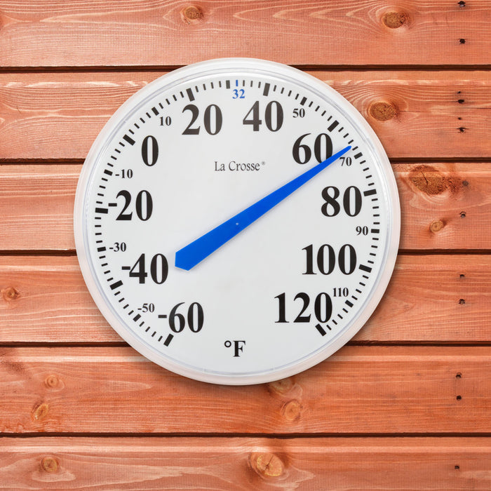 The 104-114A 13.5-inch dial thermometer with key hider, displaying the white dial with black numbers in degrees Fahrenheit from minus 60 to 120 degrees and a blue pointer highlighting freezing at 32 degrees shown hanging on a cedar color board wall or shed reading 67 degrees