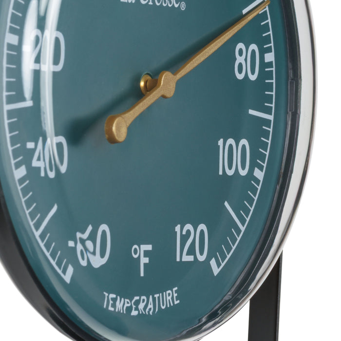 Close-up of the dial and lens of the 104-1512F 5-inch Dial Thermometer with Bracket features an emerald green dial with white temperature readings in a Fahrenheit scale from -60 to 120 degrees, with an antique gold pointer shown with the mounting bracket/stand positioned at the bottom