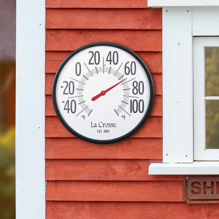 104-3056 Emperor Size 22-inch Dial Thermometer reading 66 degrees Fahrenheit  hanging on a red wood slat shed with white trim with a peak of a window and the yard in the background