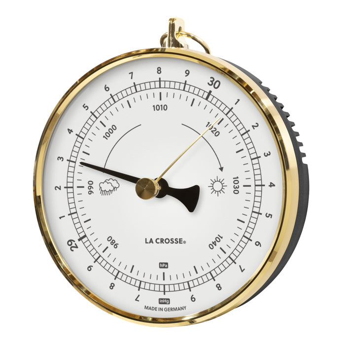 Left-facing image of the 138-1611W Analog Barometer - White featuring a brass case with a dome lens covering a white dial, brass reference marker, a black pressure indicator, black numbers, icons, and text. The barometer measures the atmospheric pressure in Hectopascals (hPa) and in Inches of Mercury (inHg) Made in Germany.