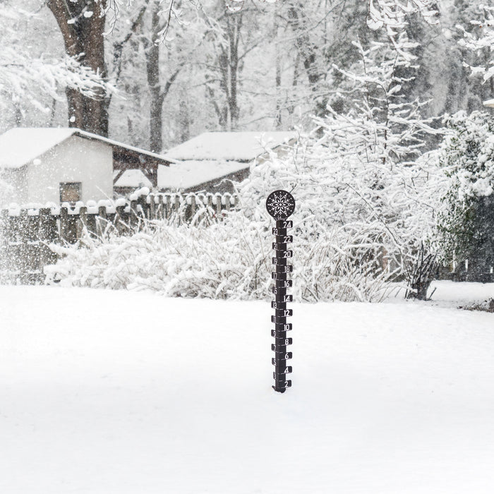 Lifstyle image of a snowy backyard with snow covered trrees, fencing, and house in the background with the 139-4686 Metal snowgague in the foreground