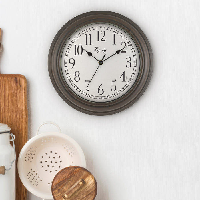 Lifestlye image of the 20898 Cora 12-inch Wall Clock hanging on a kitchen wall with kitchen gadgets. The clock features a classic dial, black numbers, seconds indicator ring, and an oil-rubbed bronze frame