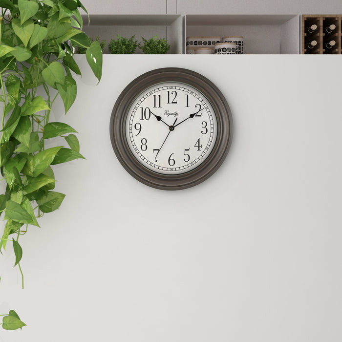Lifestlye image of the 20898 Cora 12-inch Wall Clock hanging on a white wall with shelves above the clock and a green plant. The clock features a classic dial, black numbers, seconds indicator ring, and an oil-rubbed bronze frame
