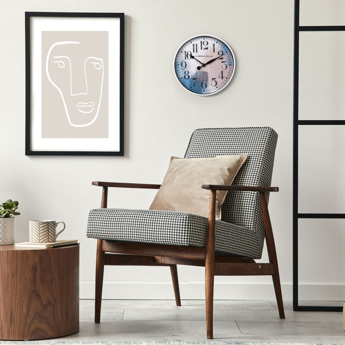 11 inch 404-3028A Brushstroke wall clock with a white case that surrounds a painted brush design dial in blues creams and taupe with black numbers and metal hands on a tan wall with modern art hanging above a houndstooth chair in black tans and creams