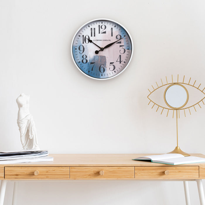Brushstroke 404-3028A 11 inch wall clock featuring a white case surrounding a painted brush design dial in blues creams and taupe black numbers and black metal hands hanging on a wall above a side table desk and a white statue and mirror eyeball decoration