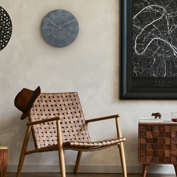 404-3028B Cormac 11 inch open face molded dark gray wall clock with numbers in relief and silver metal hour and minute hands hanging on a tan wall with a map of Paris over a rattan brown chair and side table