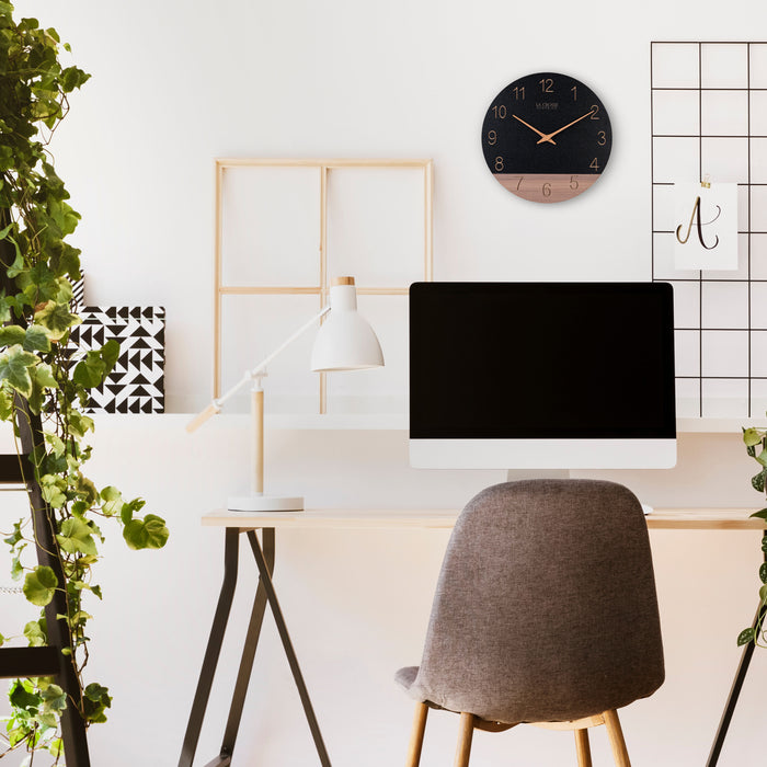 Lifestyle image of the 404-3630C 12-inch Sierra Wood Wall Clock - Black shown hanging over a desk in a home office setting. The clock featureas a black and wood split design open-face dail, with laser cut numbers, and wood hour and minutue hands.