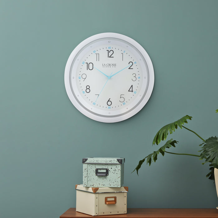 404-4525 white wall clock with blue hands shown in a daytime lifestyle on a green wall