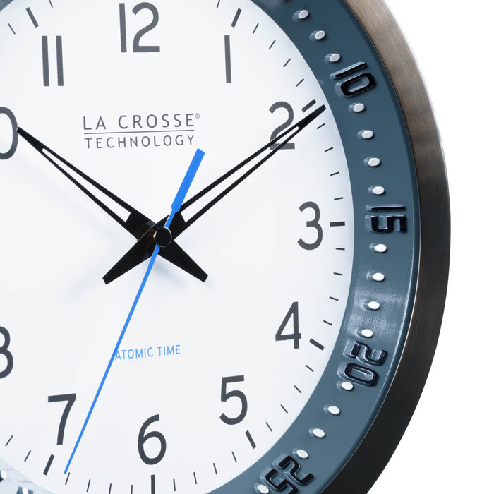 Close-up image of the dial of the 404-54667 10-inch Atomic Metal Wall Clock with Blue Chapter Ring. The clock features a black stainless steel frame with a blue chapter ring and raised seconds indicators, surrounding a white dial with black numbers, metal hands, and a blue accent second hand.