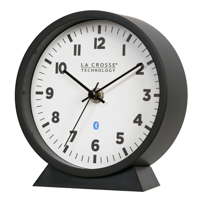 Left-facing image of the 437-3816 Insta-Set Table/Wall Clock with Bluetooth® Technology featuring a white dial with bold black numerals, black metal hands, and a black frame with removable base for tabletop or wall hanging placement.