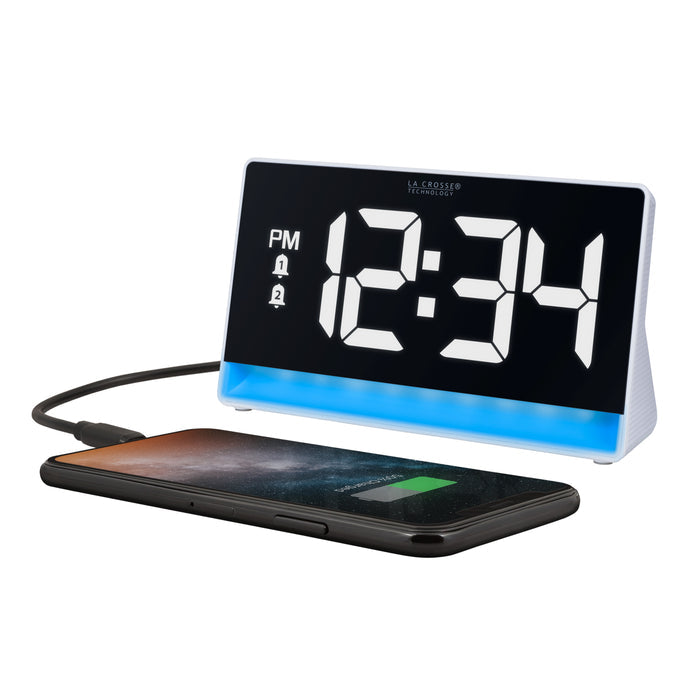Left-facing image of the 617-149 Digital Alarm Clock with Color Changing Glow Light shown with a smartphone plugged in to be charged. The alarm clock features a white case, a color-changing bar as the base, and a black display with white digits.
