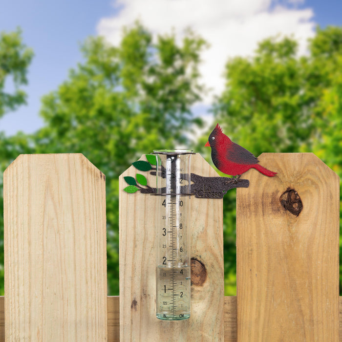 Lifestyle image of the 704-4612 Metal Cardinal rain gauge on a fence with a blue sky and trees in the background
