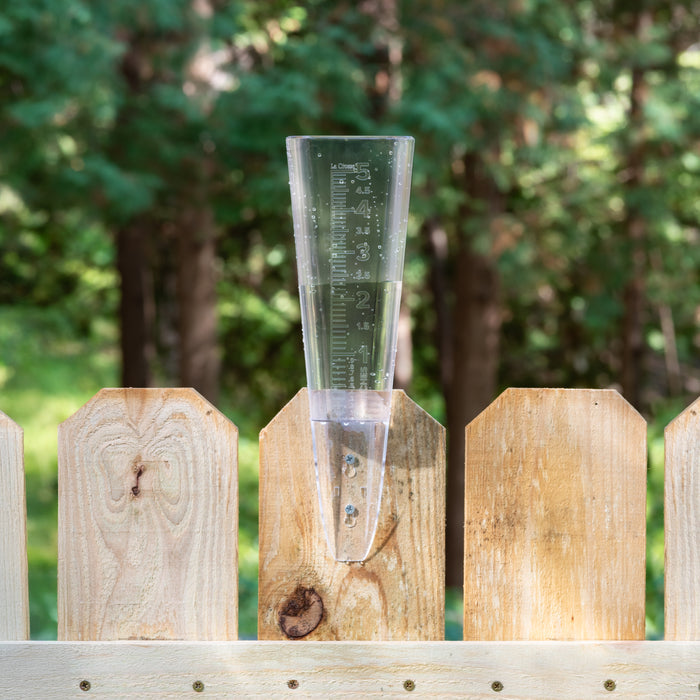 Lifestyle image of the La Crosse 704-5331 Clear measure rain gauge screwed into a wooden fence, showcasing over two inches of water collection in a backyard wooded area.