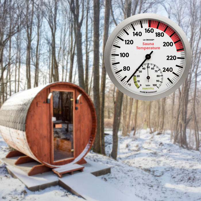 Lifestyle image of an outdoor Sauna in the winter with a backdrop of trees. Highlighting the 914-612 Sauna Thermometer with Hygrometer that features a slimline silver frame, black temperature readings (65 to 255 degrees Fahrenheit), and a hygrometer reading relative humidity %RH 0 to 100 percent.