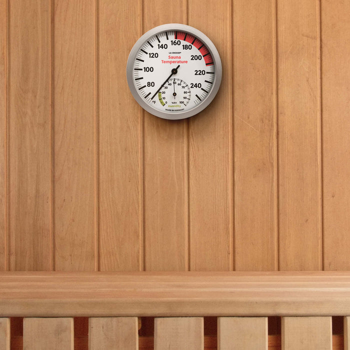 Lifestyle image inside a cedar board sauna with the 914-612 Sauna Thermometer with Hygrometer hanging on the wall above a bench. The thermometer features a slimline silver frame, black temperature readings (65 to 255 degrees Fahrenheit and a hygrometer displays the humidity readings in relative humidity %RH from 0 to 100 percent (optimal range in green 0 to 20 percent) relative humidity with a black pointer.