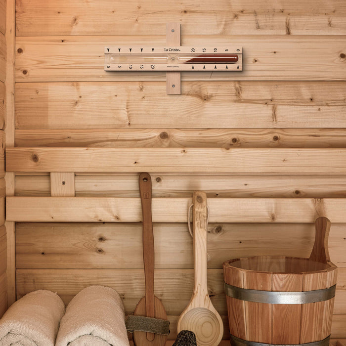 Lifestyle image inside a sauna with the 918-631 Sauna Hourglass Timer showing the wood casing, glass tube, and red sand with markings 0 to 20 minutes and the La Crosse logo in a horizontal position showing the mounting bracket attached to the wall